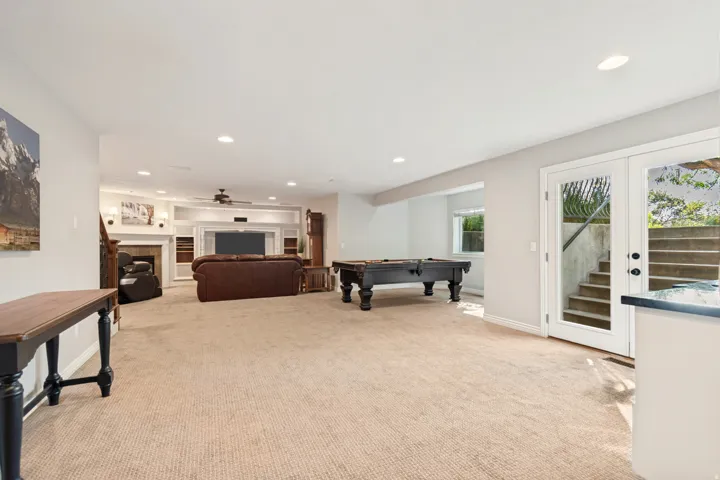 Spacious lower-level area with recessed lighting, built-in media center, fireplace, and glass French doors leading to exterior stairs