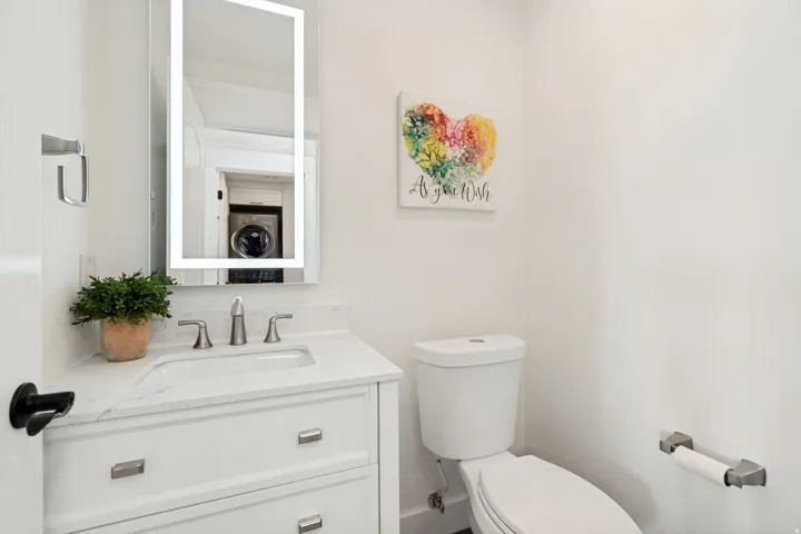 White vanity with integrated sink, brushed nickel faucet, illuminated mirror, and a white toilet