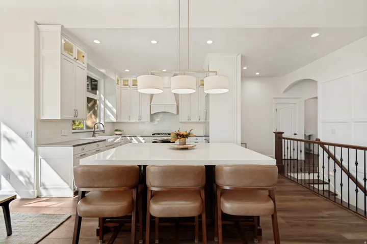 Open-concept kitchen and dining area featuring white cabinetry with integrated appliances, quartz countertops, pendant lighting, and a large waterfall-edge island