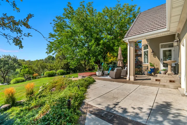 Expansive concrete patio with a covered outdoor sitting area, stucco exterior, and a sloped lawn with mature landscaping