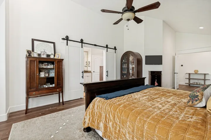 Spacious primary bedroom featuring hardwood flooring, a ceiling fan with dark wood blades, and a black metal barn-style sliding door leading to an ensuite area