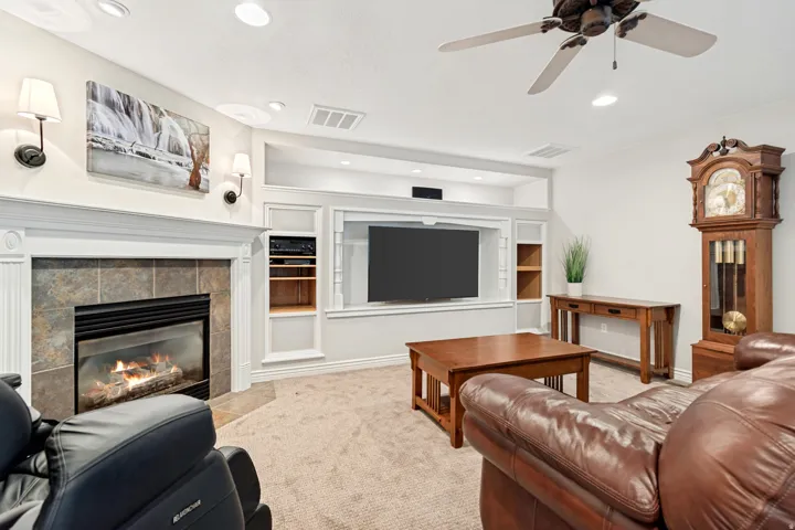 Stone-clad fireplace with a white mantel, built-in media center with shelving, recessed lighting, wall sconces, and a ceiling fan