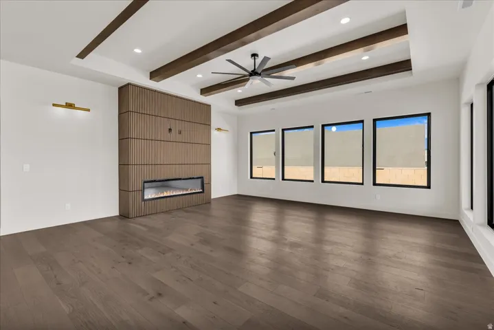 Spacious living area showcasing dark wood-finish flooring, exposed wooden ceiling beams, and a ceiling fan