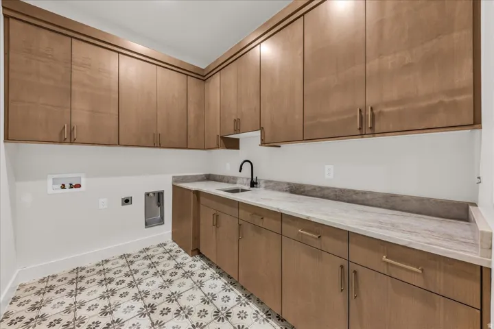 Extensive wood-finish cabinetry, solid surface countertops, integrated sink with matte black faucet, and patterned floor tile