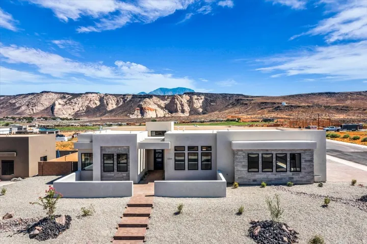 Modern exterior design with flat roof architecture, stone accent walls, multiple windows, an integrated entryway, and a decorative landscape