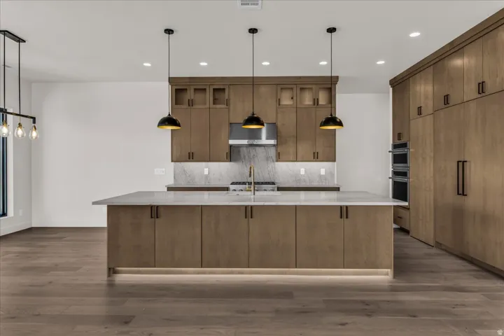 Gourmet kitchen featuring a large central island with integrated lighting, wood-finish cabinetry, stainless steel appliances, and wood-finish flooring