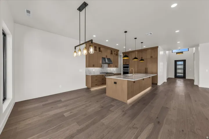 Open-concept kitchen and living area featuring warm wood-finish cabinetry, a large island with seating, stainless steel appliances, pendant lighting, and wide-plank wood-finish flooring throughout
