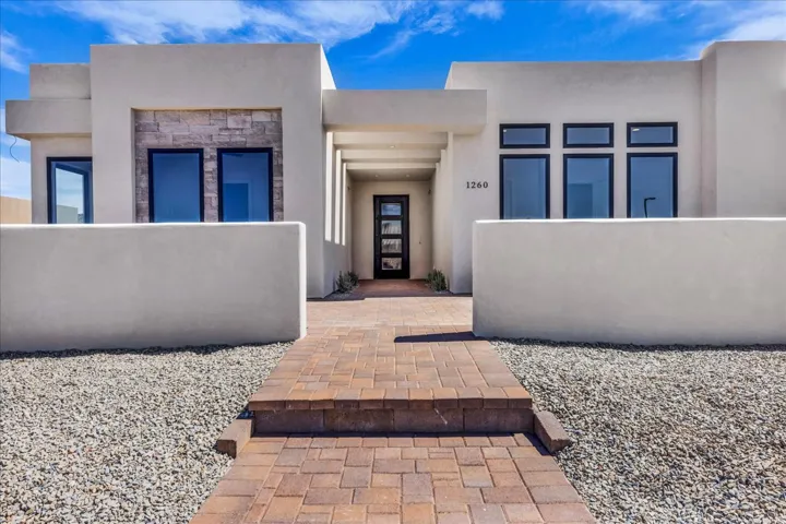 Modern stucco exterior with stone accents, featuring a paver walkway, an entry door with frosted glass panels, and multiple black-framed windows