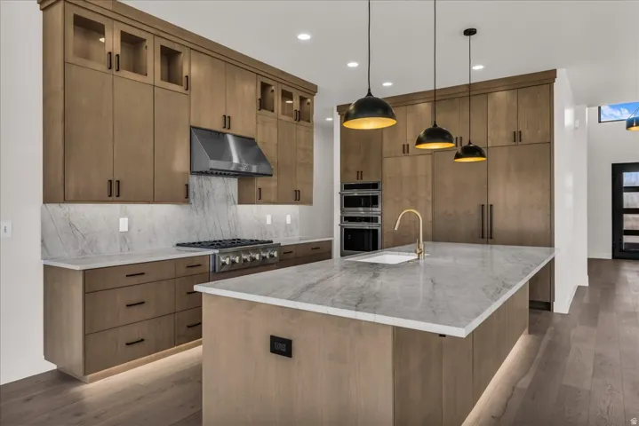 Chef's kitchen featuring custom wood-finish cabinetry with glass-front upper storage, marble-look countertops, a large center island with waterfall edge, professional-grade gas cooktop, stainless steel appliances, and pendant lighting suspended above the