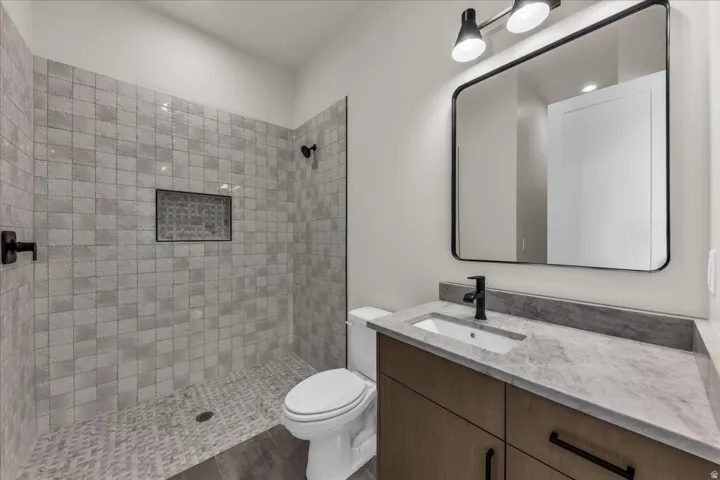 Walk-in shower with tiled walls and floor, built-in recessed shelf, vanity with integrated sink, stone countertop, and wood-finish cabinetry