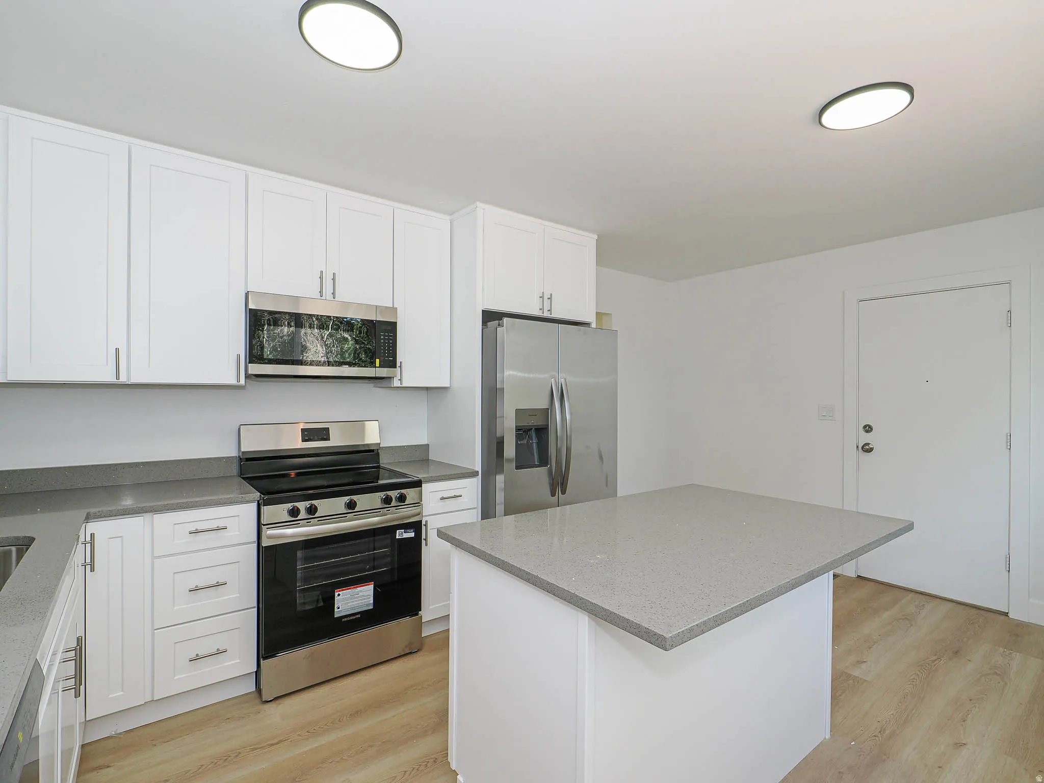 Kitchen featuring white cabinetry, stainless steel appliances, light-toned wood-finish flooring, a kitchen island, and gray countertops