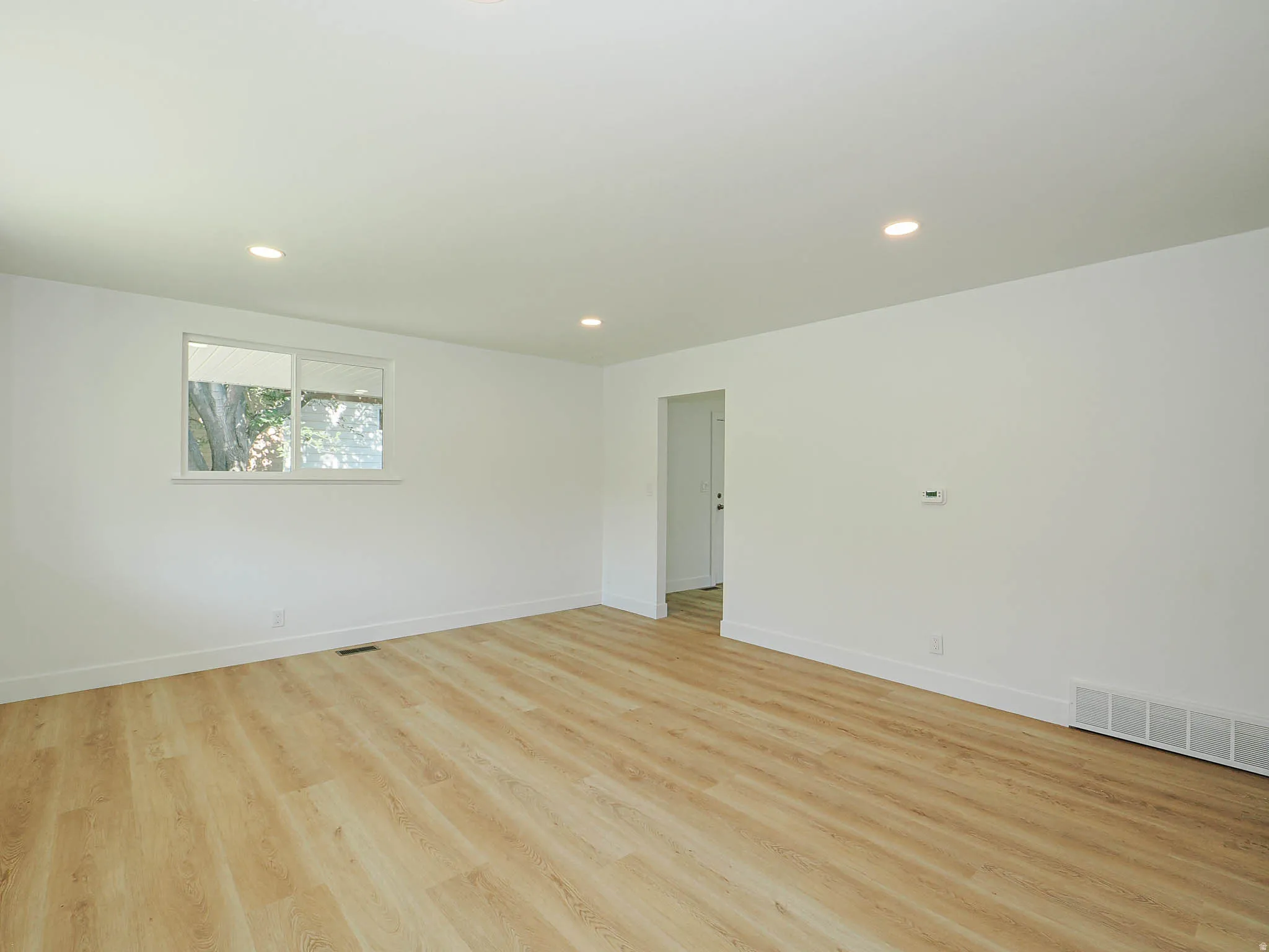 Recessed lighting, wood-finish flooring, white walls, and a window with a white frame