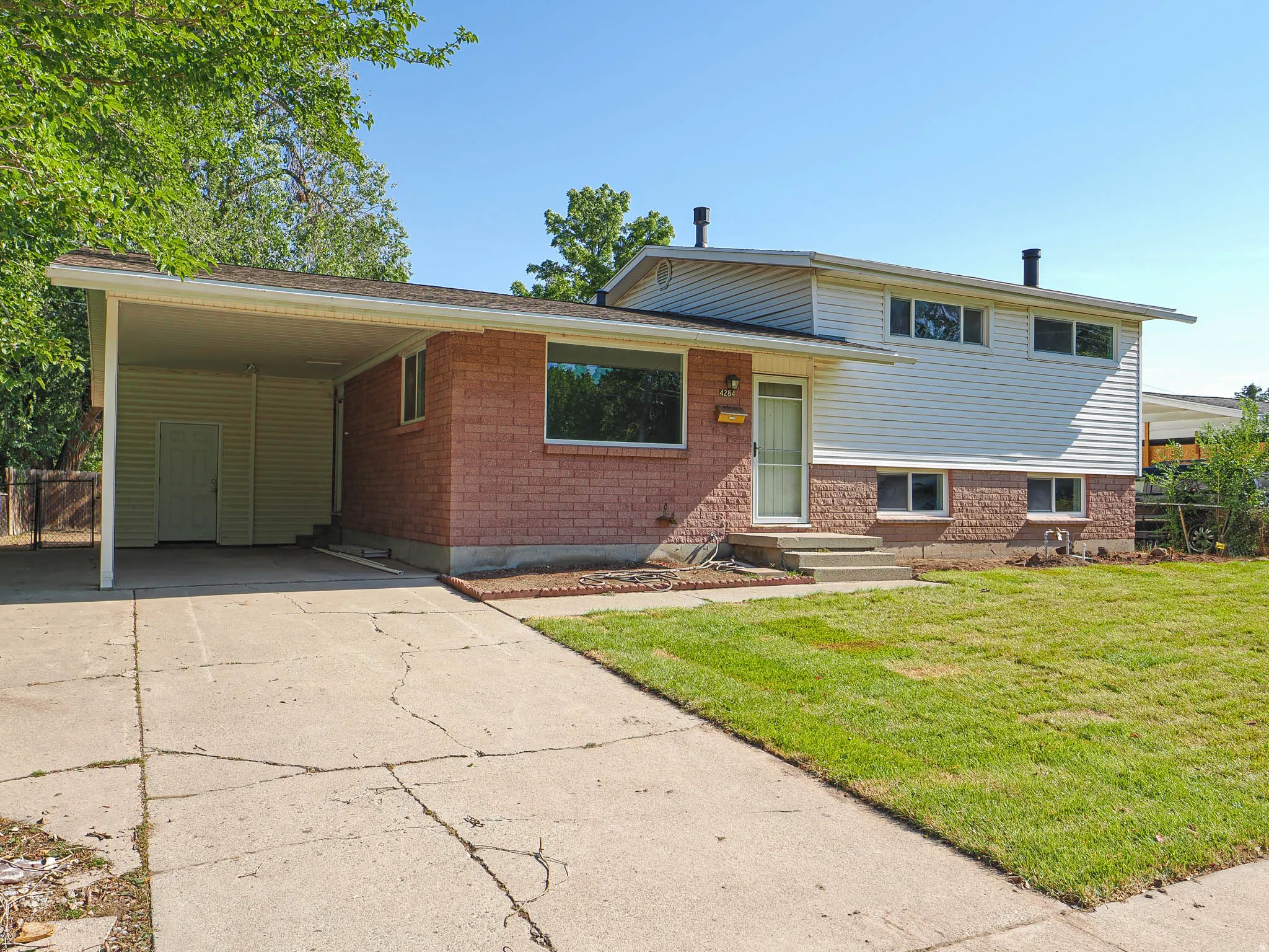 Brick and siding exterior with a covered carport, concrete driveway, and a front lawn