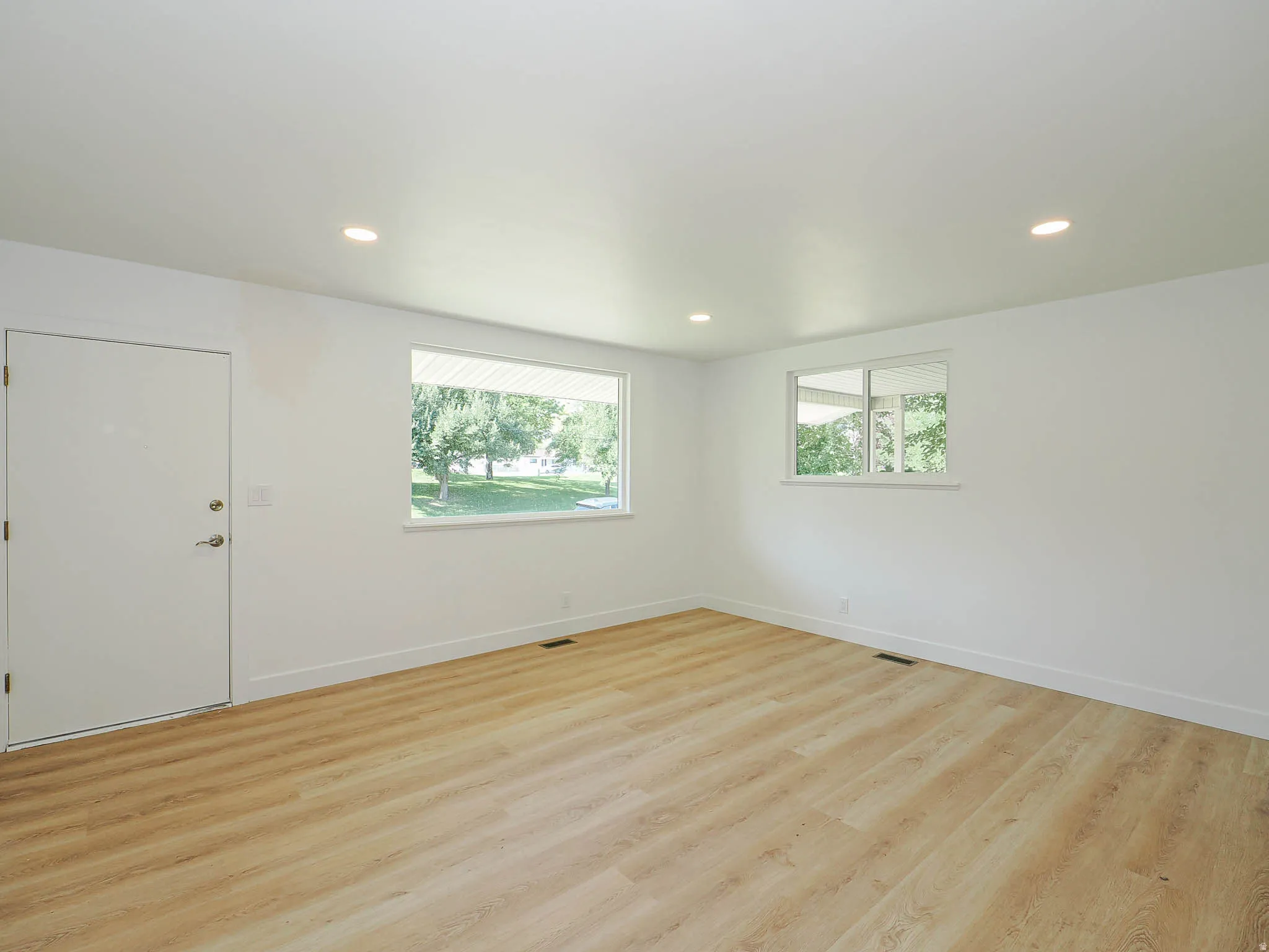 Recessed lighting illuminates the open area with light wood-finish flooring