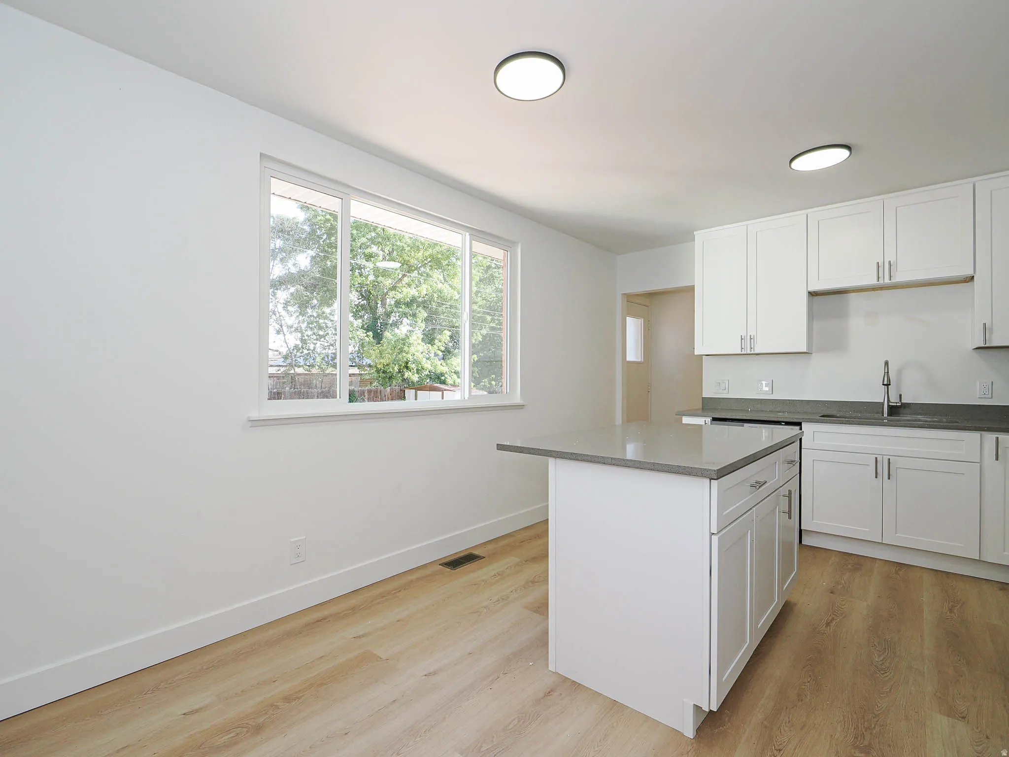 Kitchen featuring white shaker cabinetry, an island with countertop seating, wood-finish flooring, and a stainless steel sink with a gooseneck faucet