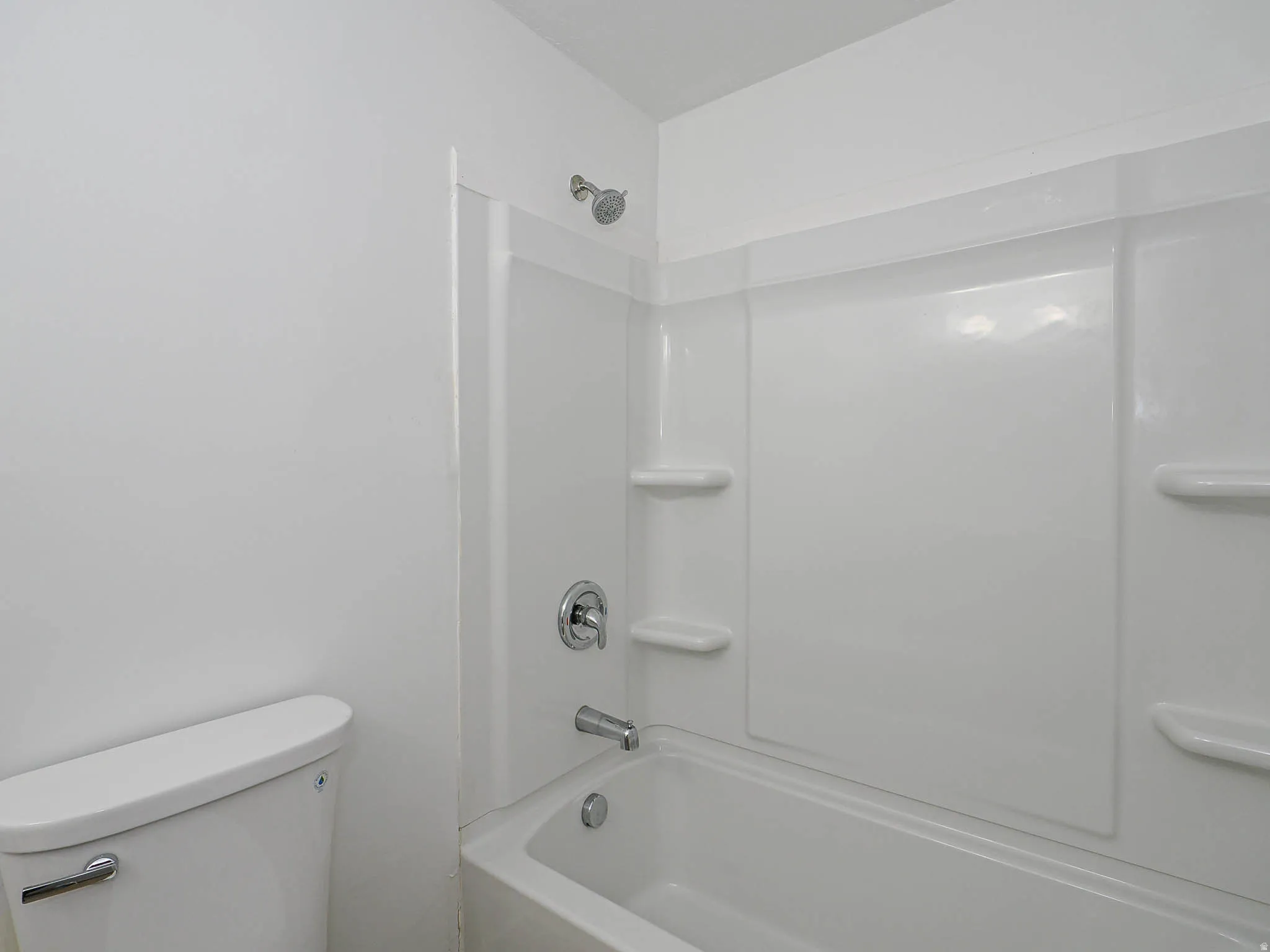 White bathtub with integrated shower, chrome fixtures, and built-in shelving