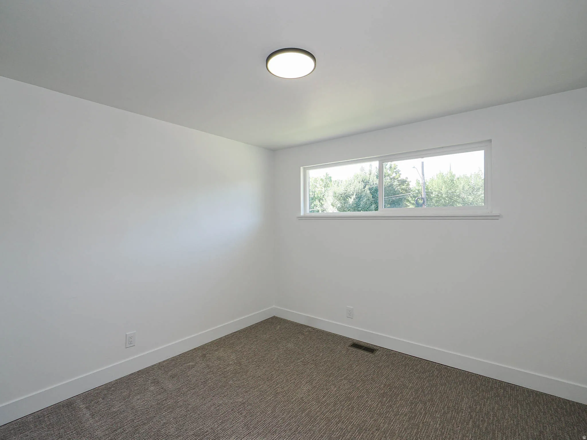 White walls, rectangular window, light-colored ceiling, flush-mount ceiling light fixture, and textured carpet flooring