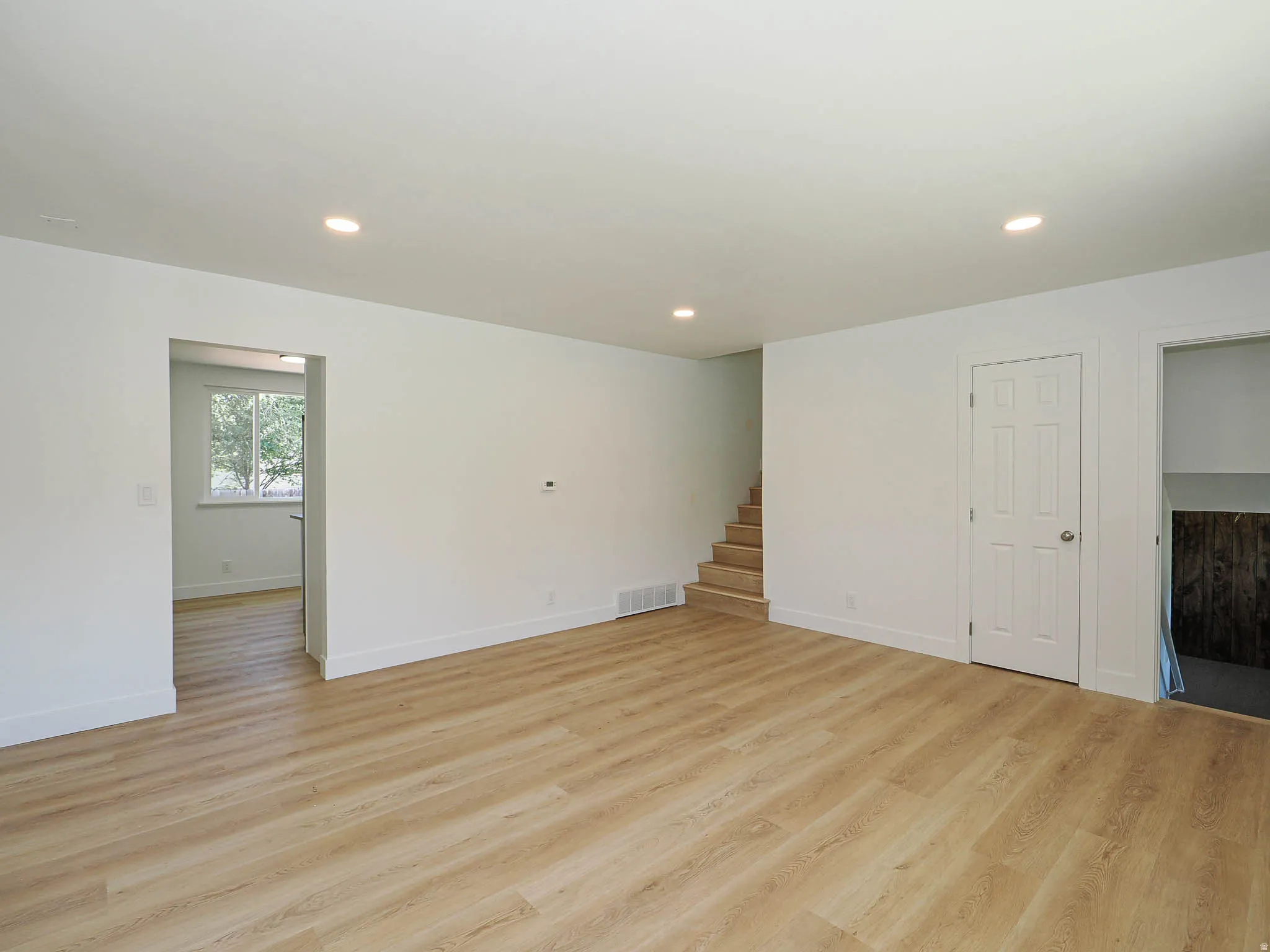 Wood-finish flooring, recessed lighting, white interior walls, interior staircase, and a paneled interior door