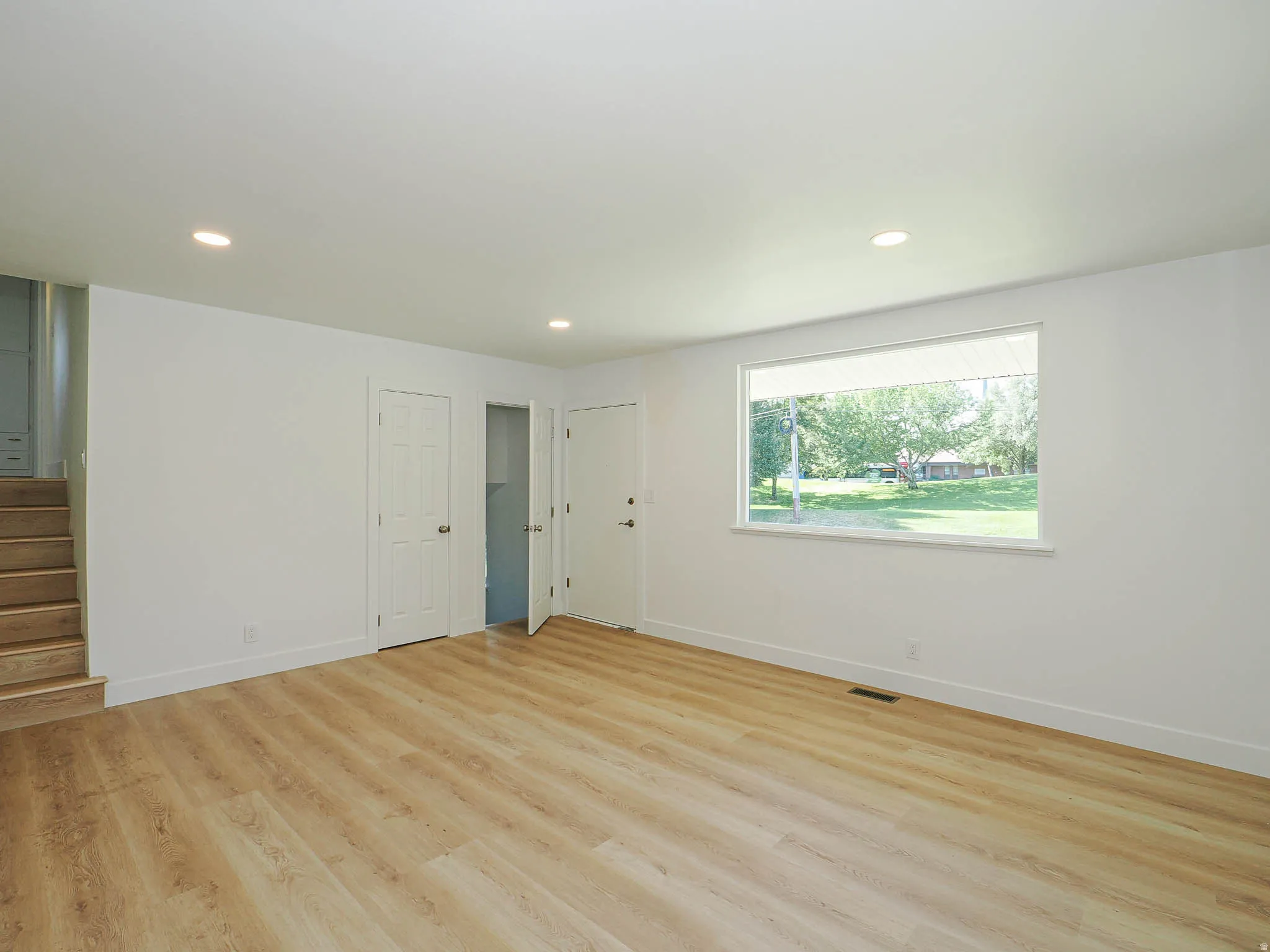 Bright, open room featuring gleaming wood-finish flooring, recessed ceiling lighting, and multiple white panel doors
