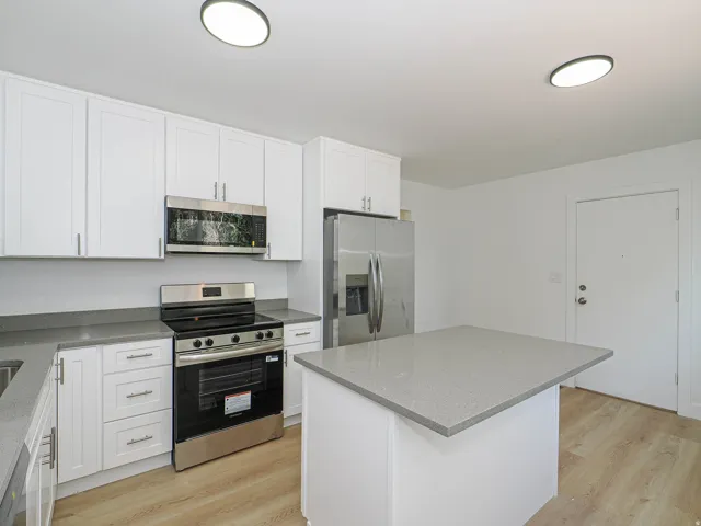 Kitchen featuring white cabinetry, stainless steel appliances, light-toned wood-finish flooring, a kitchen island, and gray countertops