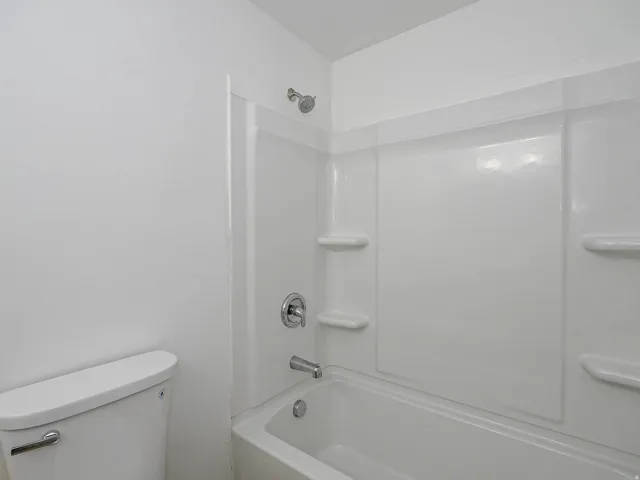 White bathtub with integrated shower, chrome fixtures, and built-in shelving