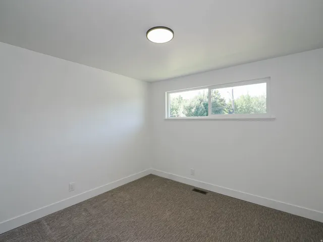 White walls, rectangular window, light-colored ceiling, flush-mount ceiling light fixture, and textured carpet flooring