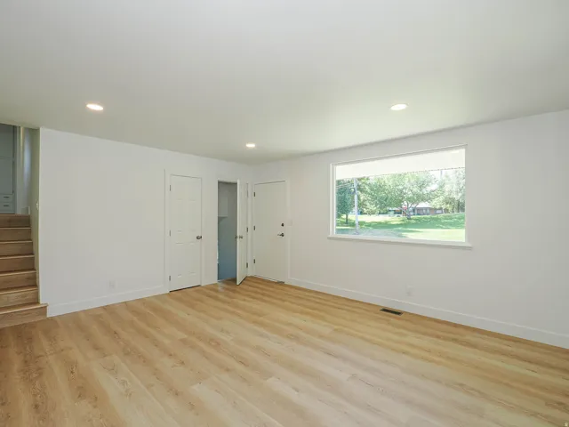 Bright, open room featuring gleaming wood-finish flooring, recessed ceiling lighting, and multiple white panel doors