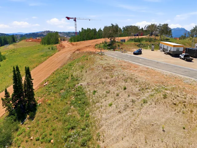 Expansive undeveloped lot featuring a paved road frontage, natural landscaping with mature trees, and mountainous terrain