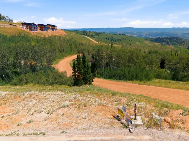 Scenic mountain landscape featuring a winding dirt road, scattered trees, and distant hills