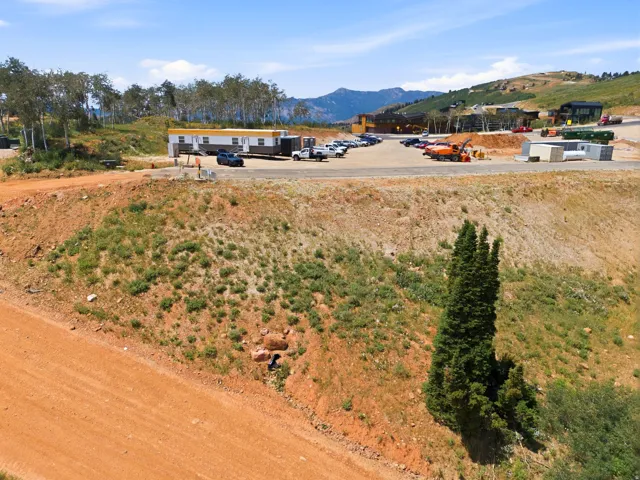 Undeveloped mountain terrain featuring a red dirt road, sparse green vegetation, and distant mountain views