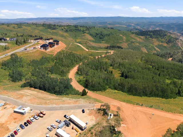 Expansive mountain landscape featuring varied terrain, a winding unpaved road, and distant residential structures
