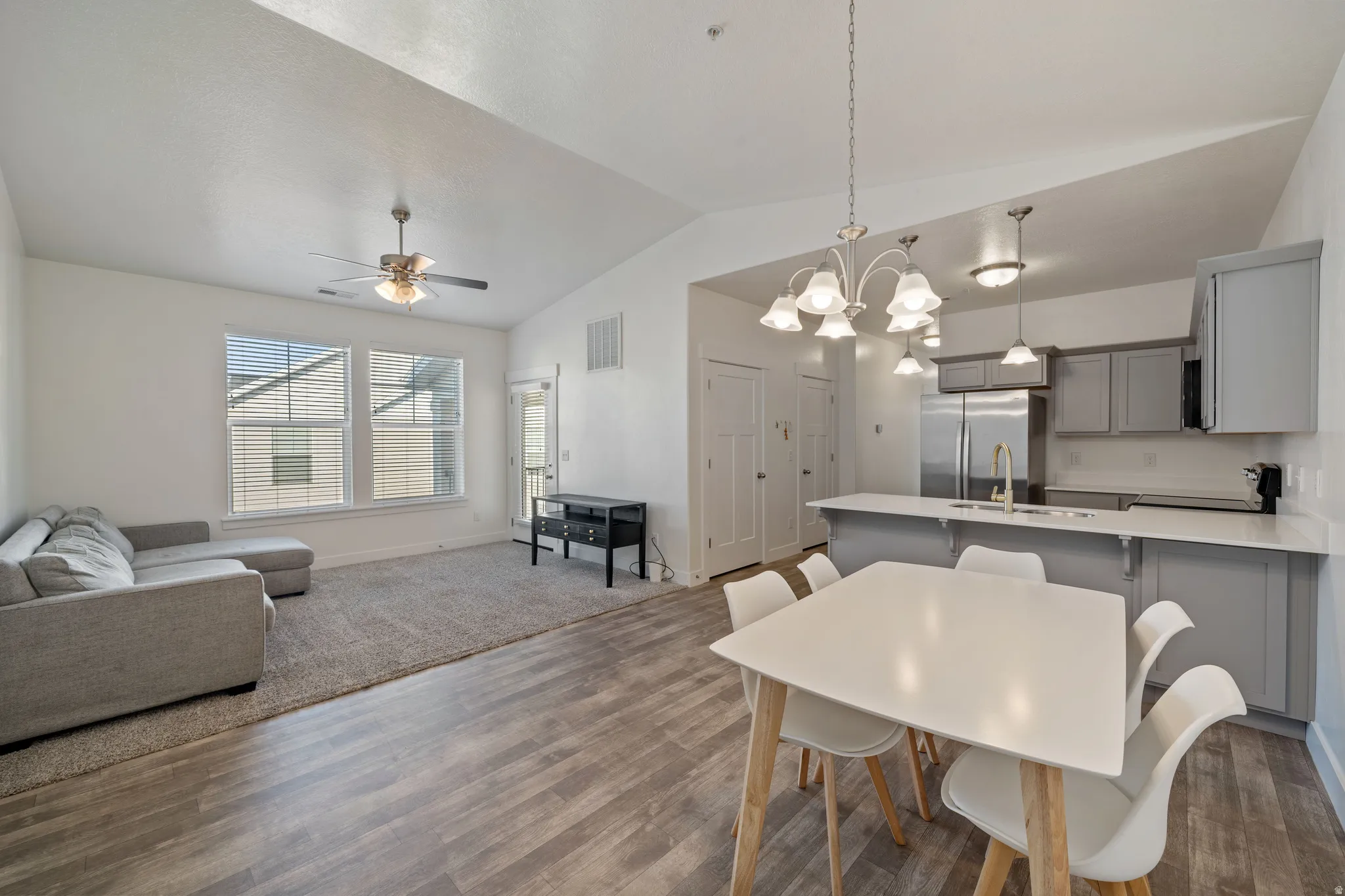 Open-concept living area featuring LVP flooring throughout, a dining space with a white table and natural wood legs, a gray upholstered sofa, and a modern kitchen with gray cabinetry, stainless steel appliances, and a white quartz countertop