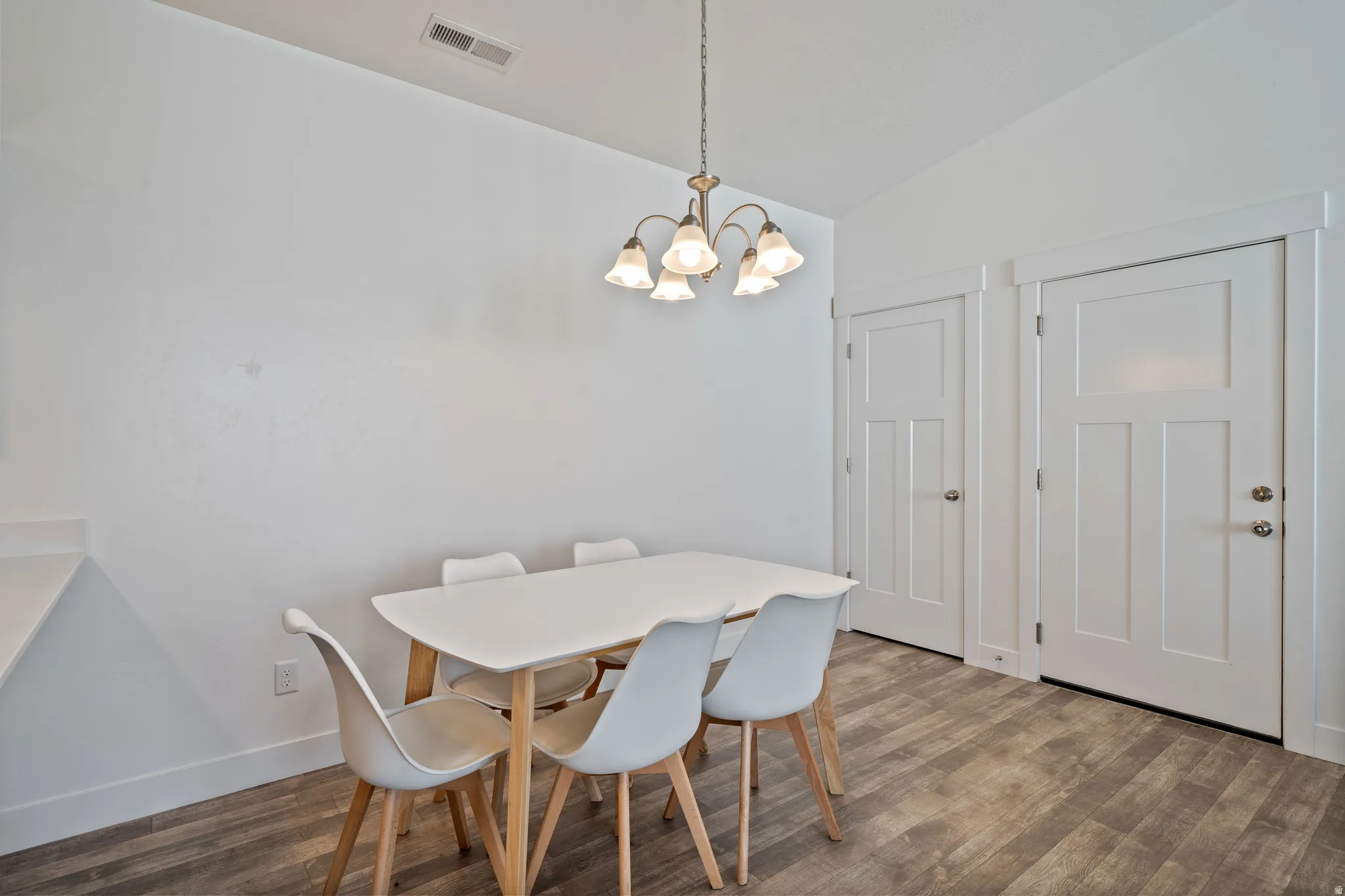 Bright dining space featuring a wood-finish table with seating for four, warm pendant lighting fixture, and wood-finish flooring throughout