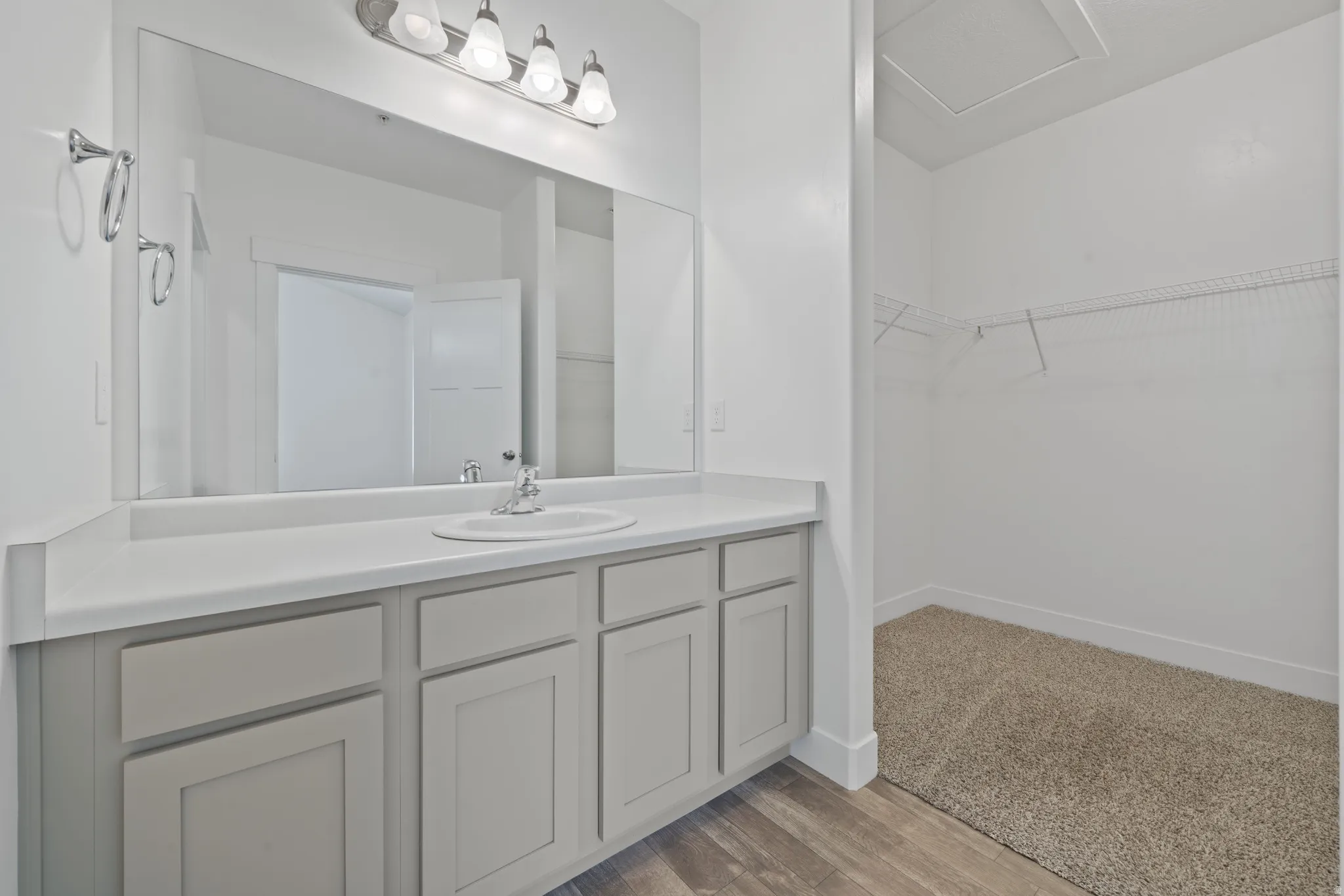 Primary Bathroom with Dual Vanity Featuring Spacious Quartz Countertop, Gray Cabinetry with Recessed Paneling, Large Framed Mirror with Integrated Lighting, Walk-In Shower with Subway Tile Surround, and LVP Flooring