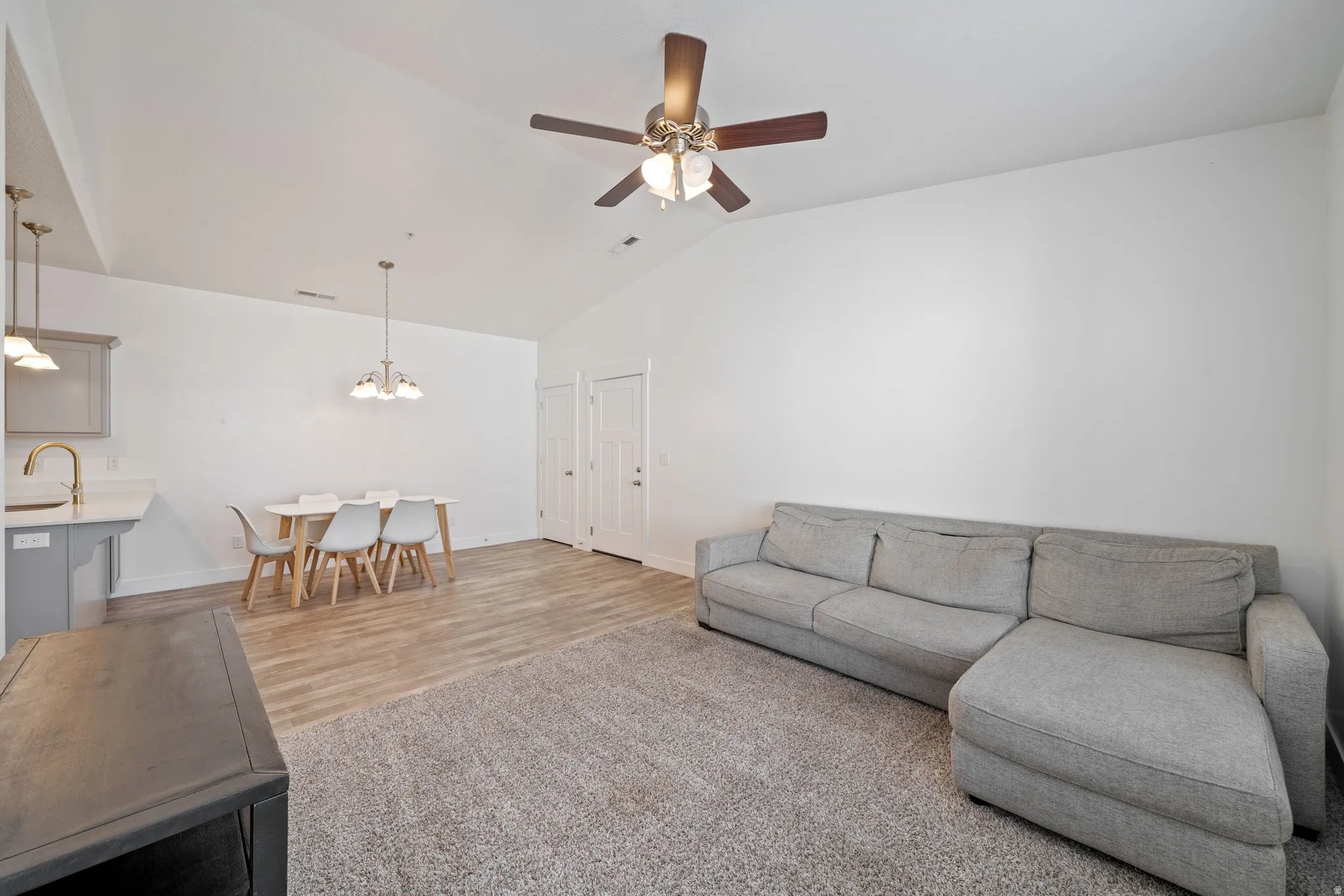 Open-concept living area featuring warm wood-finish flooring, a gray upholstered sectional sofa, and a ceiling fan with brass accents