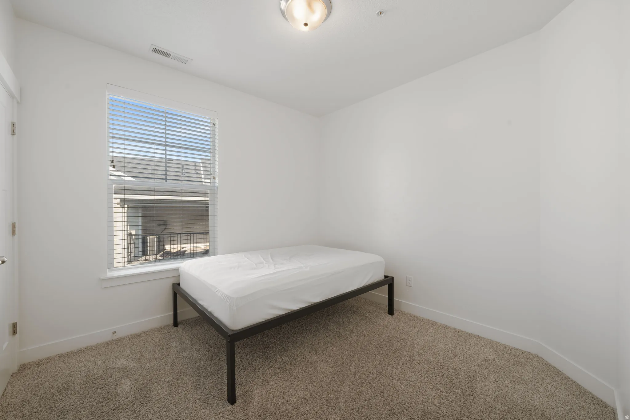 Bright secondary bedroom featuring a large double-hung window with plantation shutters, neutral wall finishes, and carpet flooring throughout
