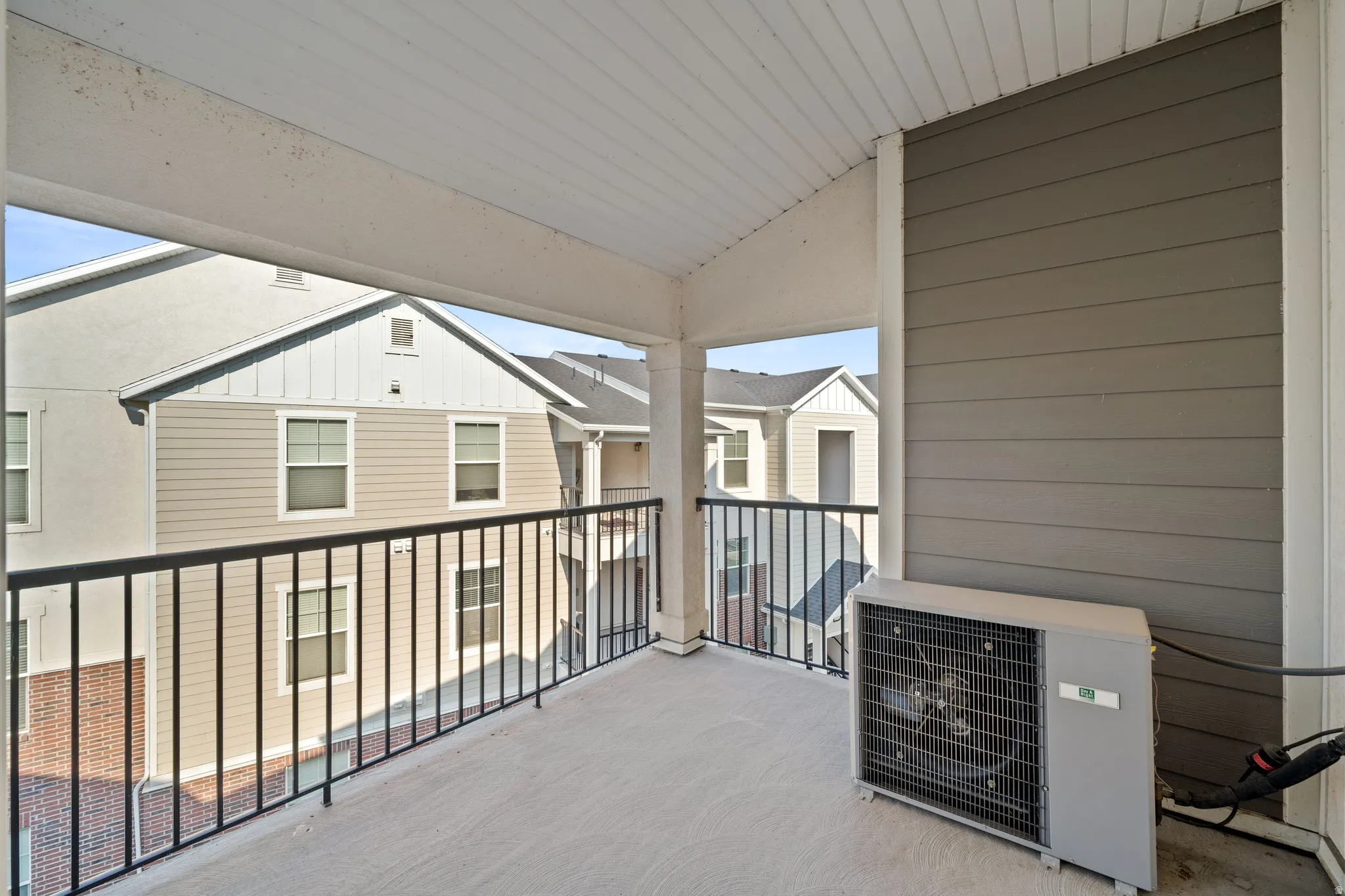 Covered top level deck featuring metal railing, composite decking, and a ceiling with linear soffits