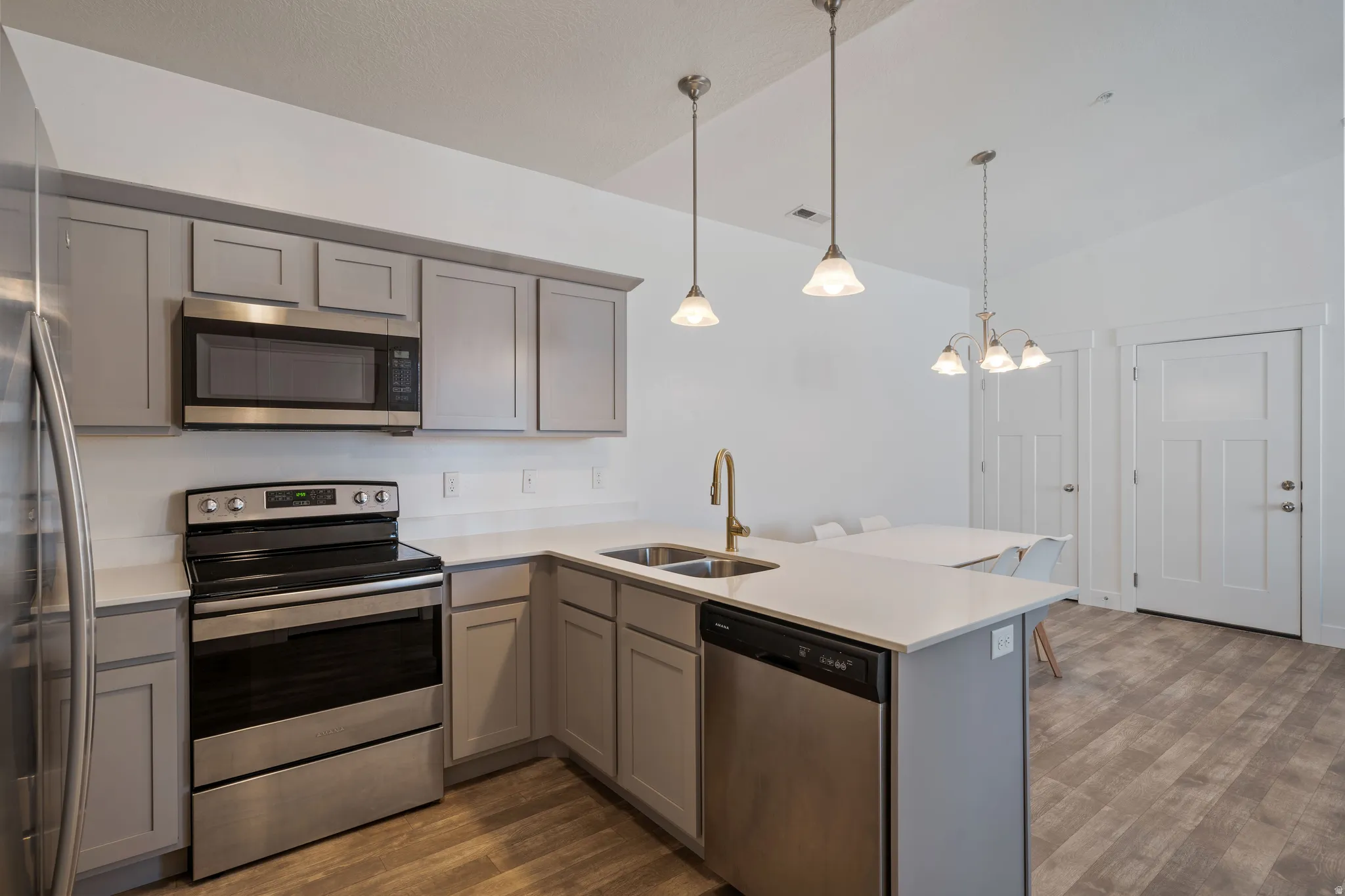 Modern kitchen featuring stainless steel appliances, including a gas range and microwave, paired with gray cabinetry and a white quartz island countertop