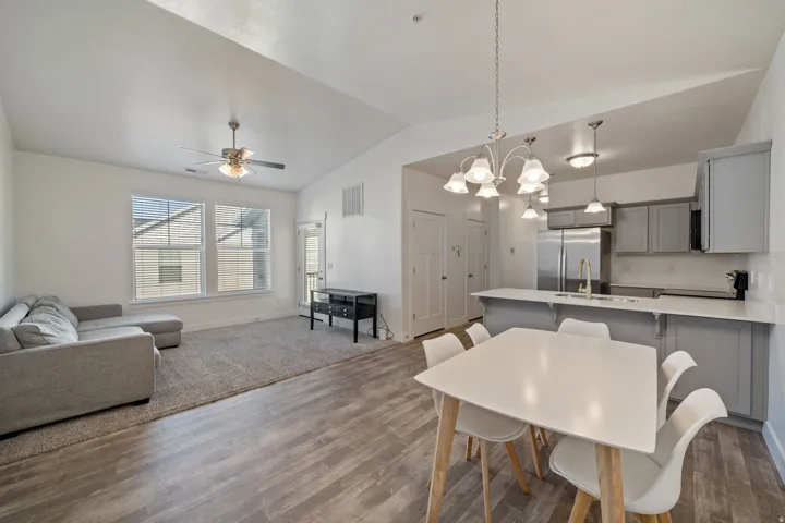 Open-concept living area featuring LVP flooring throughout, a dining space with a white table and natural wood legs, a gray upholstered sofa, and a modern kitchen with gray cabinetry, stainless steel appliances, and a white quartz countertop