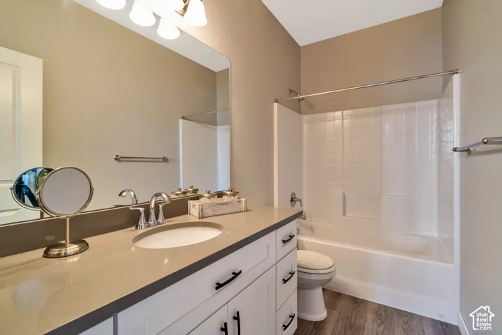 Spacious bathroom featuring a white vanity with dark hardware, an integrated sink, a large mirror, and wood-finish flooring