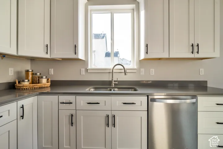 Kitchen featuring white shaker-style cabinetry, dark countertops, a stainless steel sink with a gooseneck faucet, and a stainless steel dishwasher