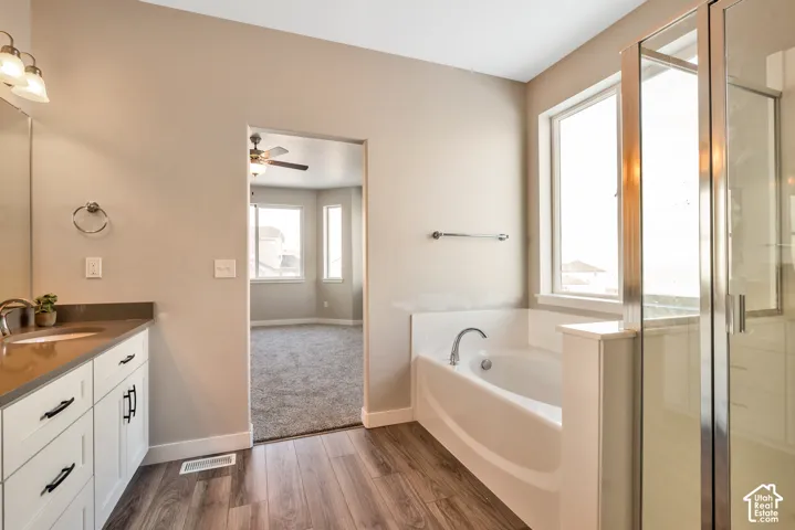 Wood-finish flooring, white vanity with dark countertop, built-in bathtub, and a glass-enclosed shower