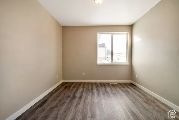 Bright, light-filled bedroom with expansive window framing natural daylight, neutral wall finishes, wood-finish flooring throughout, and recessed ceiling lighting