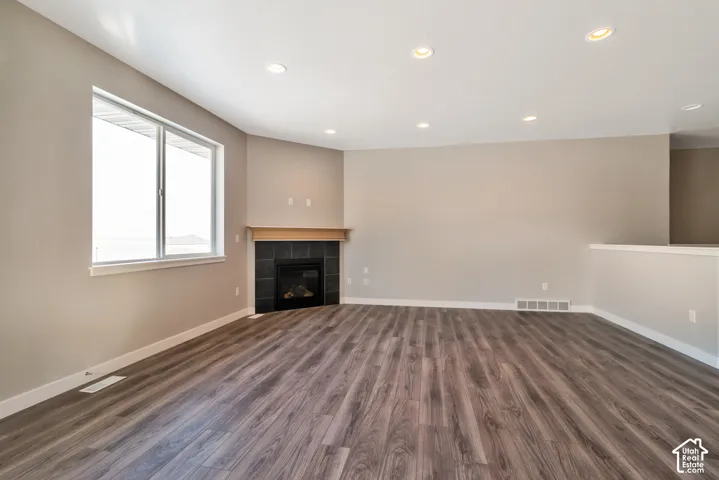 Wood-finish flooring, recessed lighting, expansive window, tiled fireplace surround, and a natural wood mantel