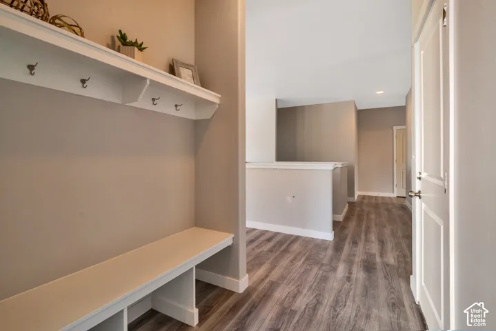Mudroom featuring built-in bench seating with storage underneath, floating shelves with integrated hooks for organization, wood-finish flooring, and neutral taupe walls with soft recessed lighting