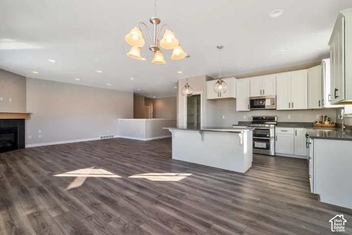 Spacious room featuring wood-finish flooring, a kitchen island with pendant lighting, white cabinetry, and stainless steel appliances