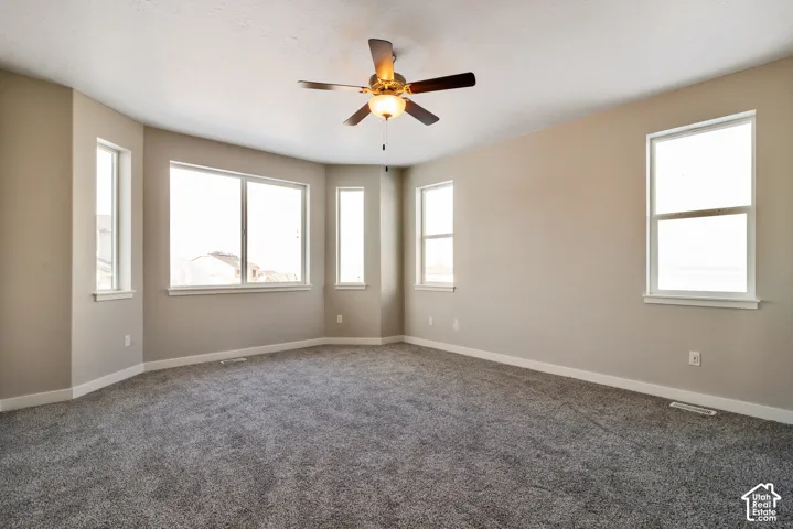 Bright corner room with abundant natural light from multiple windows, neutral wall finishes, and ceiling fan with brass fixture