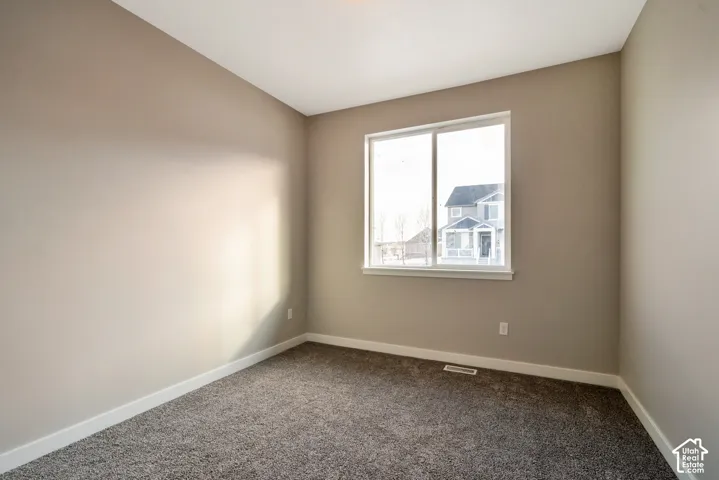 Bright corner bedroom featuring neutral wall finishes, plush carpeting, and a large double-hung window with natural light exposure