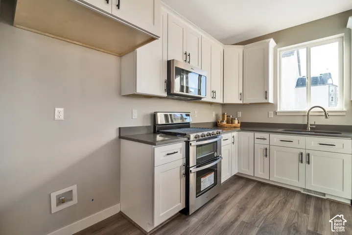 White shaker-style cabinetry, stainless steel appliances, dark countertops, a stainless steel sink with a gooseneck faucet, and wood-finish flooring