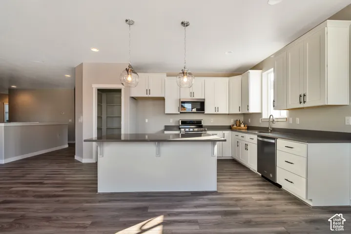 Kitchen featuring dark wood-finish flooring, white cabinetry, dark countertops, and a center island with pendant lighting